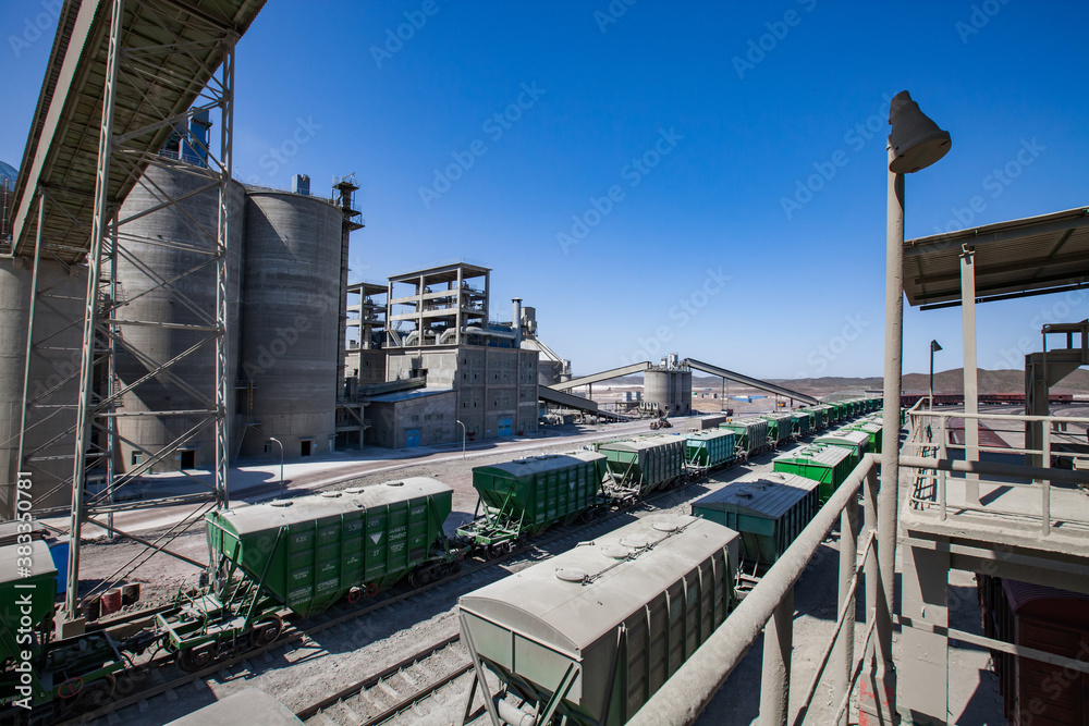 Mynaral/Kazakhstan - April 23 2012: Modern cement plant in desert. Hopper cars on loading railroad terminal. Cement silo on blue sky background.