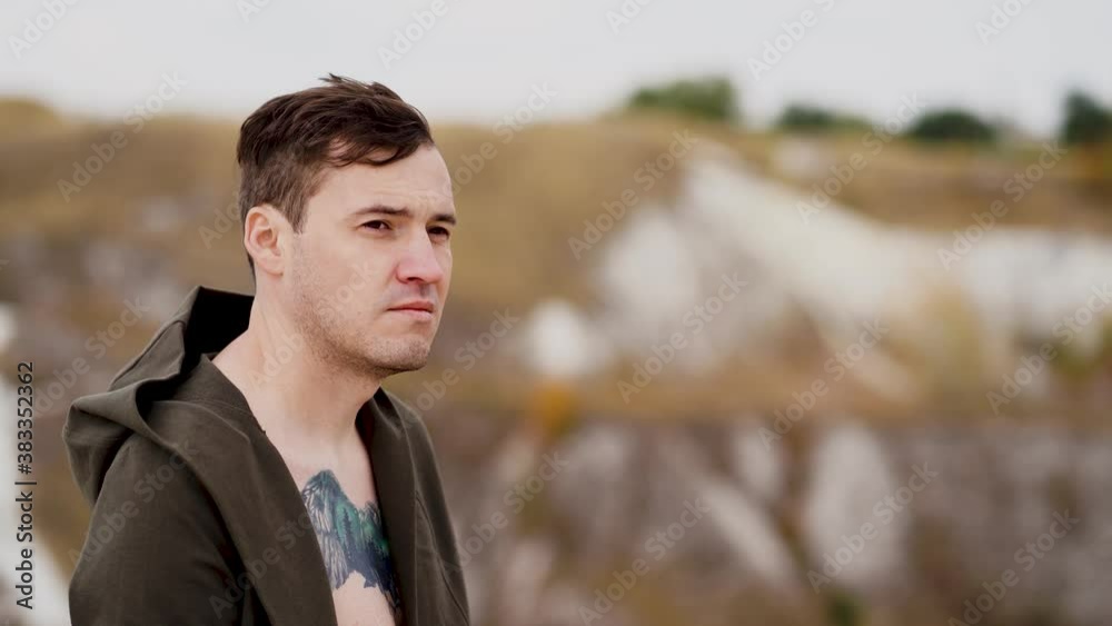 Tattooed man with bare torso in cape stands in hilly terrain. Adult male enjoys beautiful view of countryside in windy weather. Slow motion.
Tattooed man with bare torso in cape stands in hilly terrain. Adult male enjoys beautiful view of countryside in windy weather. Slow motion.