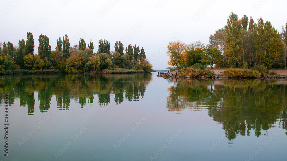 Autumn park with a river or lake. Calm and clean water surface. On the shore, people are fishing.