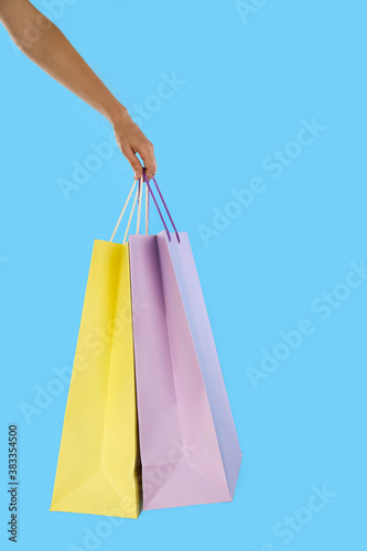 Woman with paper shopping bags on light blue background, closeup