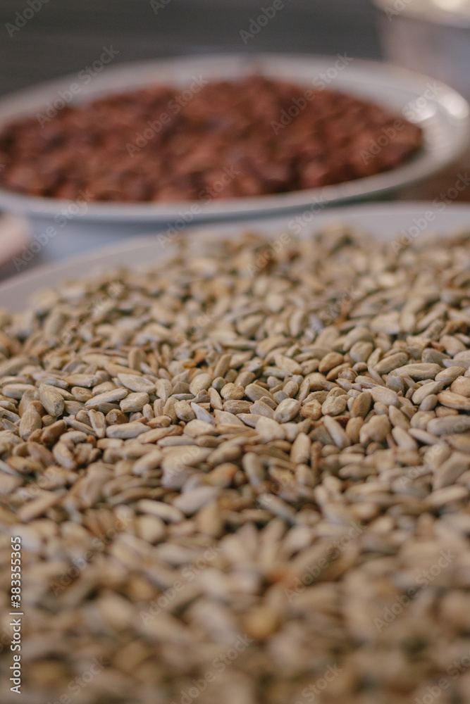 Obraz premium Roasted sunflower seeds in a plate in the foreground and peanuts in the background. Close-up.Macro shot. Selective focus.