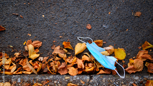 Blue Disposable Face Mask Discarded onto Street by Autumn Leaves.
