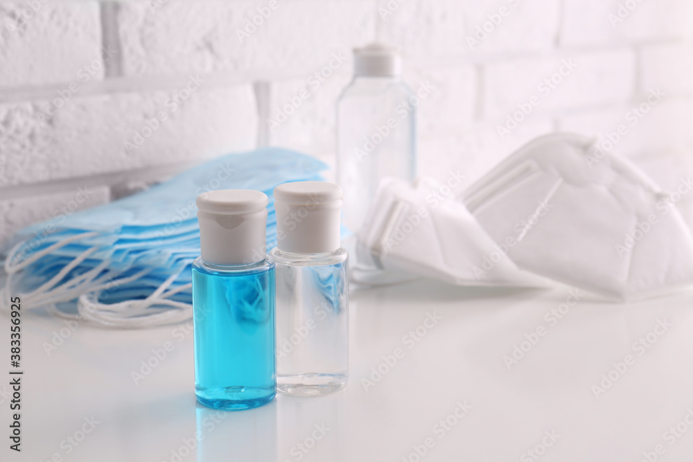 Hand sanitizers and respiratory masks on table near white brick wall. Protective essentials during COVID-19 pandemic Hand sanitizers and respiratory masks on table near white brick wall. Protective essentials during COVID-19 pandemic