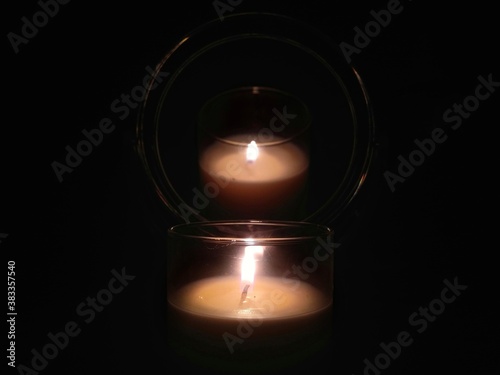 Burning white candle reflected in the mirror in the dark