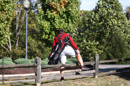A young man straddles a small fence as he walks to the next tee box.