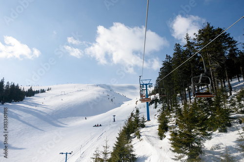 Ski piste and chair lift with snow covered trees on sunny day. Combloux ski area, French alps