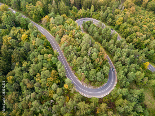 Fototapeta Naklejka Na Ścianę i Meble -  Winding road through the forest, from high mountain pass, in autumn season. Aerial view by drone. Romania