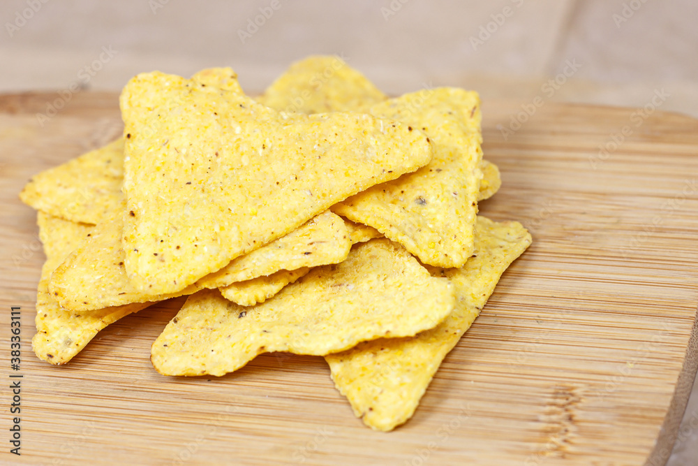 Salty crunchy and crispy triangle mexican corn nachos on light wooden background.