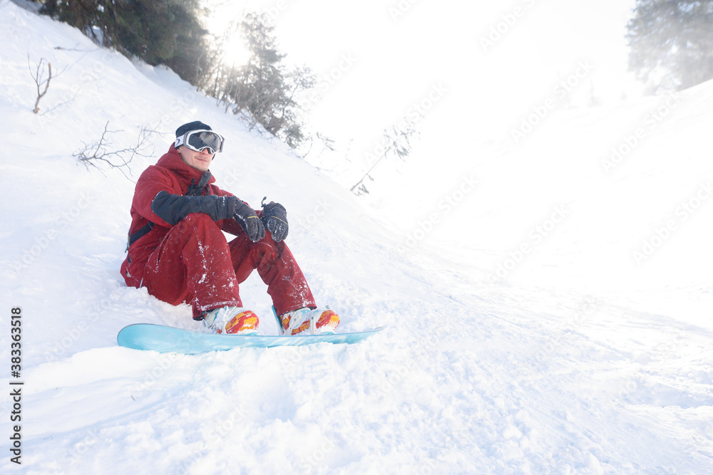 winter, leisure, sport and people concept - snowboarder sits high in the mountains on the edge of the slope and looks into the distance.