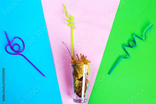 a glass with autumn leaves with acurly plastic multicolored tubules for drinks on multicolored background
