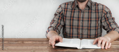 Opened Bible book in the hands of a man. Sitting at a wooden table