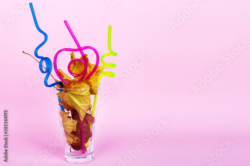 autumn leaf cocktail. autumn leaves in a glass with a straw on a pink background