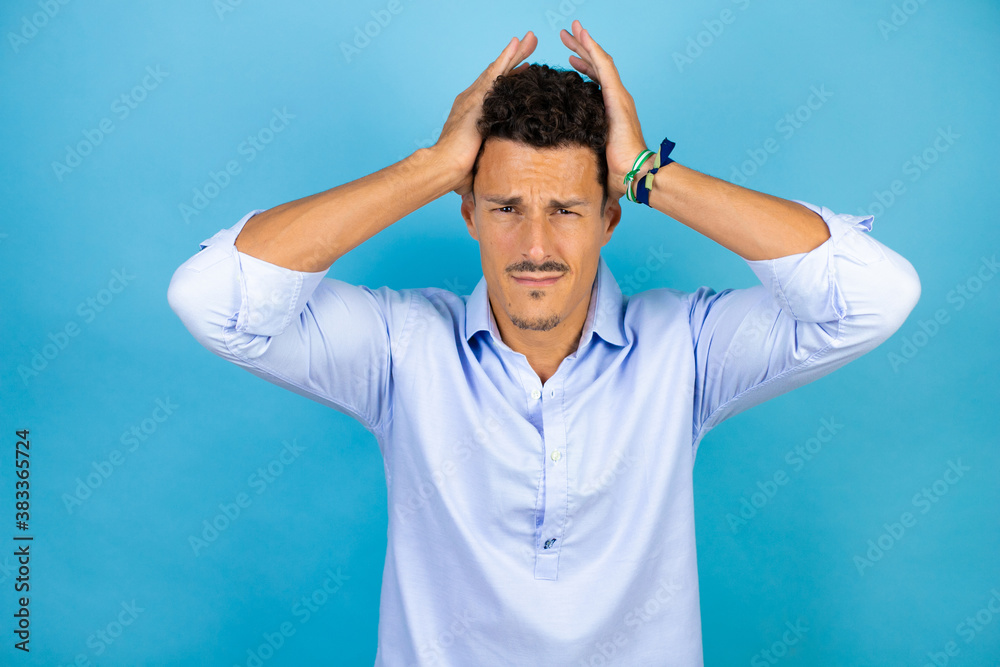 Young handsome man wearing blue shirt over isolated blue background suffering from headache desperate and stressed because pain and migraine with her hands on head Young handsome man wearing blue shirt over isolated blue background suffering from headache desperate and stressed because pain and migraine with her hands on head
