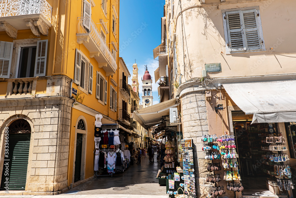 Typical old Corfu city narrow street with small shops on a foreground and clock tower on the background.