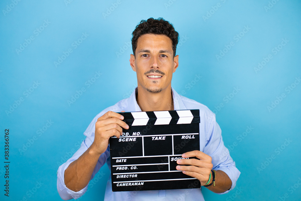 Young handsome man wearing blue shirt over isolated blue background holding clapperboard very happy
