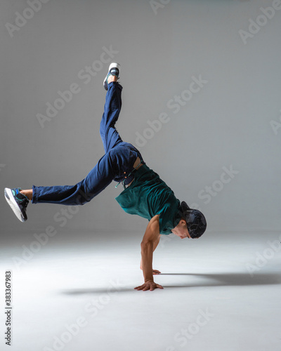 Cool guy breakdancer dances on the floor standing on hands isolated on gray background. Breakdance lessons
