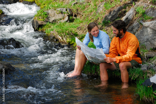 Laughing hikers check a map while soaking feet in stream