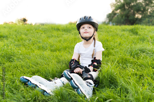 Little girl wearing inline roller skates and protective equipment outdoors