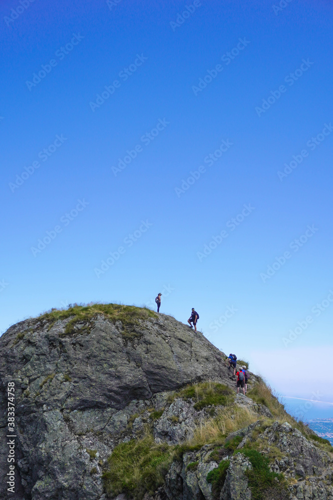 People at the top of a rocky mountain on a sunny day with a cloudless sky