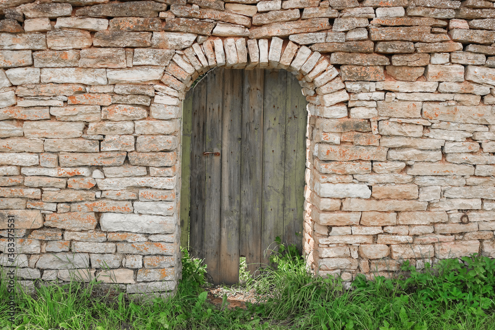 Old wooden plank door of various shades of wood, in a wall of a stone building.