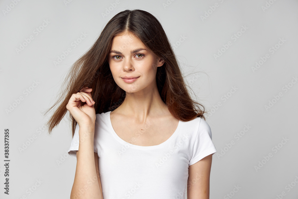 A pretty brunette in a white T-shirt holds her hand near her face and smiles A pretty brunette in a white T-shirt holds her hand near her face and smiles