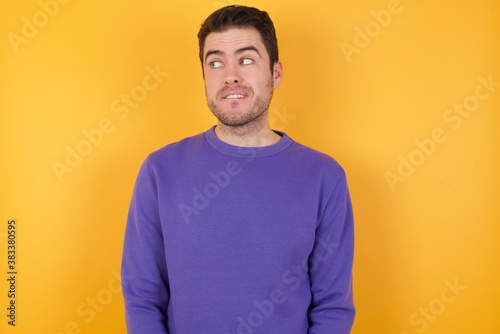 Amazed Handsome man with sweatshirt over isolated yellow background bitting lip and looking up to empty space,