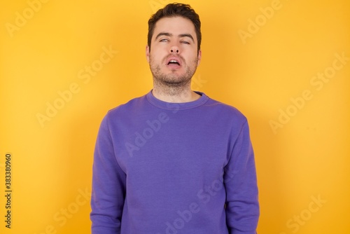 Handsome man with sweatshirt over isolated yellow background looking sleepy and tired, exhausted for fatigue and hangover, lazy eyes in the morning.