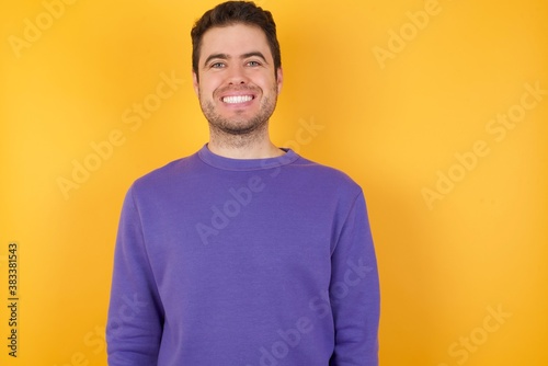 Handsome man with sweatshirt over isolated yellow background with a happy and cool smile on face. Lucky person.