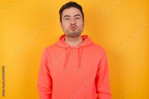 Shot of pleasant looking Handsome man with sweatshirt over isolated yellow background, pouts lips, looks at camera, Human facial expressions © Roquillo