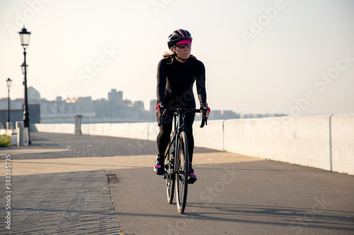 Принти на полотні Woman athlete cyclist rides a bicycle along the embankment at sunrise