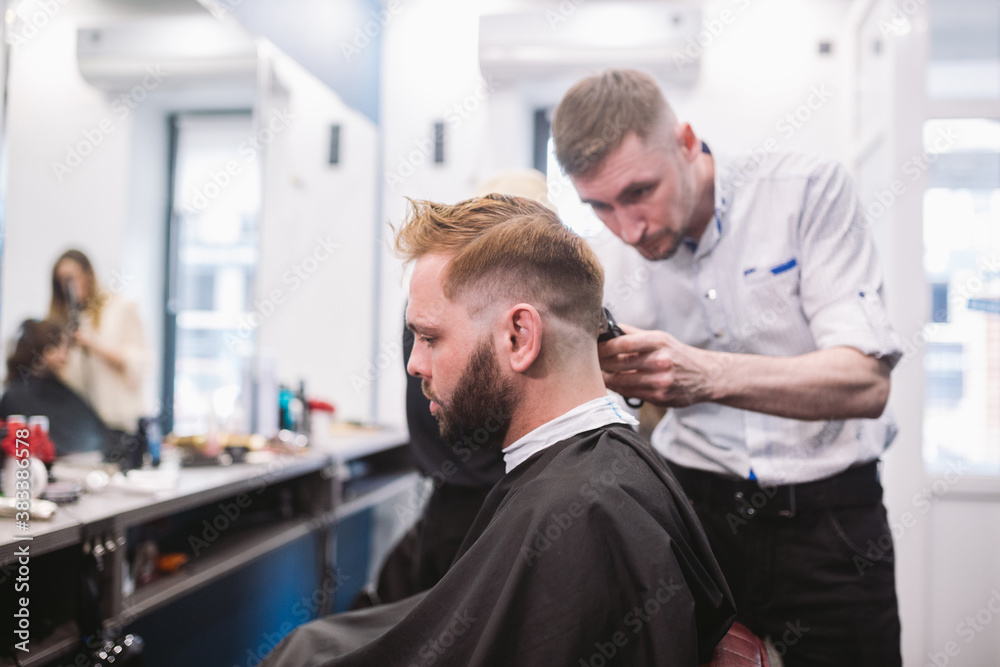 Close up shot of man getting trendy haircut at barber shop. Male hairstylist serving client, making haircut using machine and comb Close up shot of man getting trendy haircut at barber shop. Male hairstylist serving client, making haircut using machine and comb