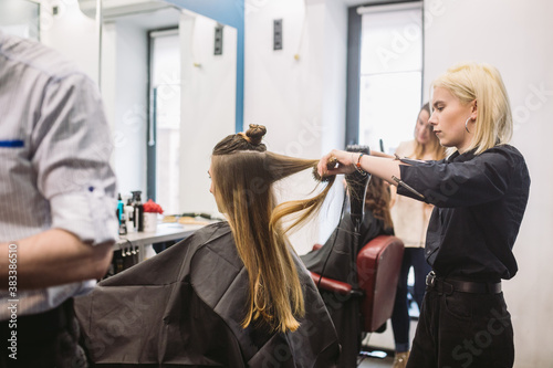 Portrait of happy woman at the hair salon. Professional hair styling concept. Hairdresser drying girl long hair using hairdryer and brush. Drying With Blow Dryer