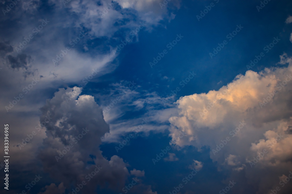 tuft of gray shaded cloud and white cumulus cloud floating side by side under a celestial blue sky sprinkled with cirrus clouds.