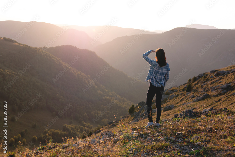 Young woman admiring sunset on the background of mountains. Hiker on a mountain top at sunset rays of the sun.