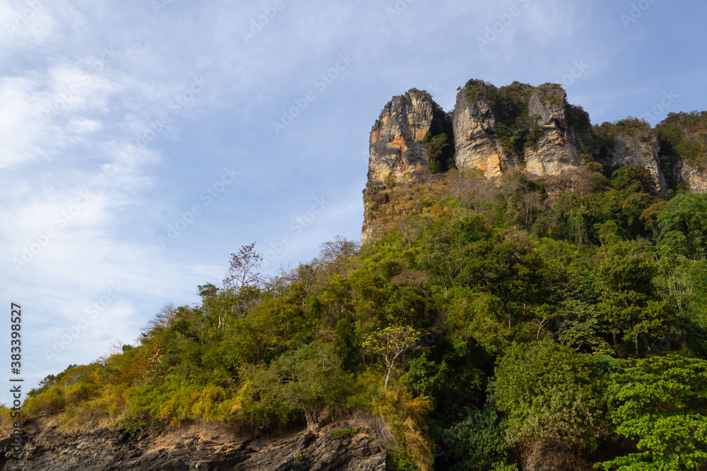 mountains and rocks covered with trees against a blue sky with clouds. Thailand