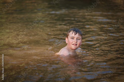 Fototapeta Naklejka Na Ścianę i Meble -  Boy swimming in river at dusk looking up at camera. Springtime fun in New South Wales, Australia
