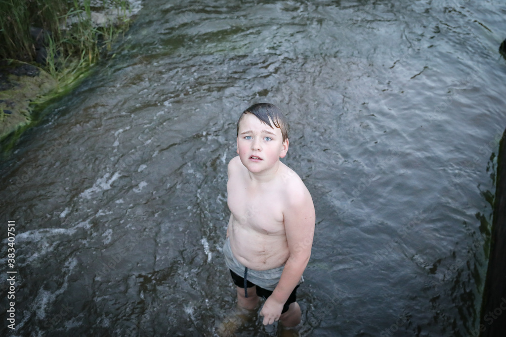 Fototapeta premium Boy swimming in river at dusk looking up at camera. Springtime fun in New South Wales, Australia