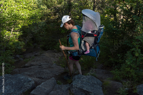 Woman hiking with baby looks to see how to navigate around rocks along a backcountry trail