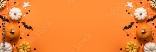 Halloween creative flat lay banner composition. Celebration decorations, bats, pumpkins and ghost on orange background, top view with copy space.