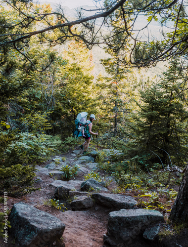 Woman hiking with baby applies pressure to two trekking poles finding her way down from the trail