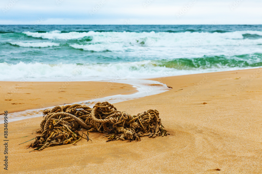 The old rope is lying on the sand on the beach against the background of the sea and waves. The old rope is lying on the sand on the beach against the background of the sea and waves.