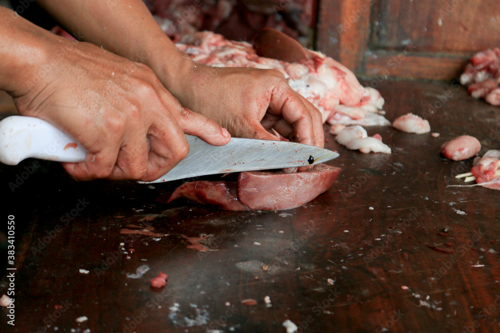 Butcher cutting raw lung or offal of cow and goat on a wooden chopping Board with knife.