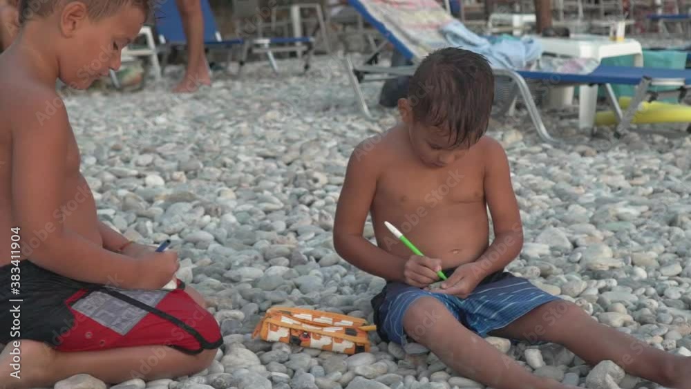 Two caucasian boys sitting on pebbles at shore of beach at Kalamata, Greece, painting them with markers 120fps Two caucasian boys sitting on pebbles at shore of beach at Kalamata, Greece, painting them with markers 120fps