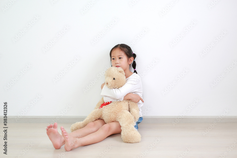 Asian little child girl hugging a teddy bear doll sitting against white wall in the room. Asian little child girl hugging a teddy bear doll sitting against white wall in the room.