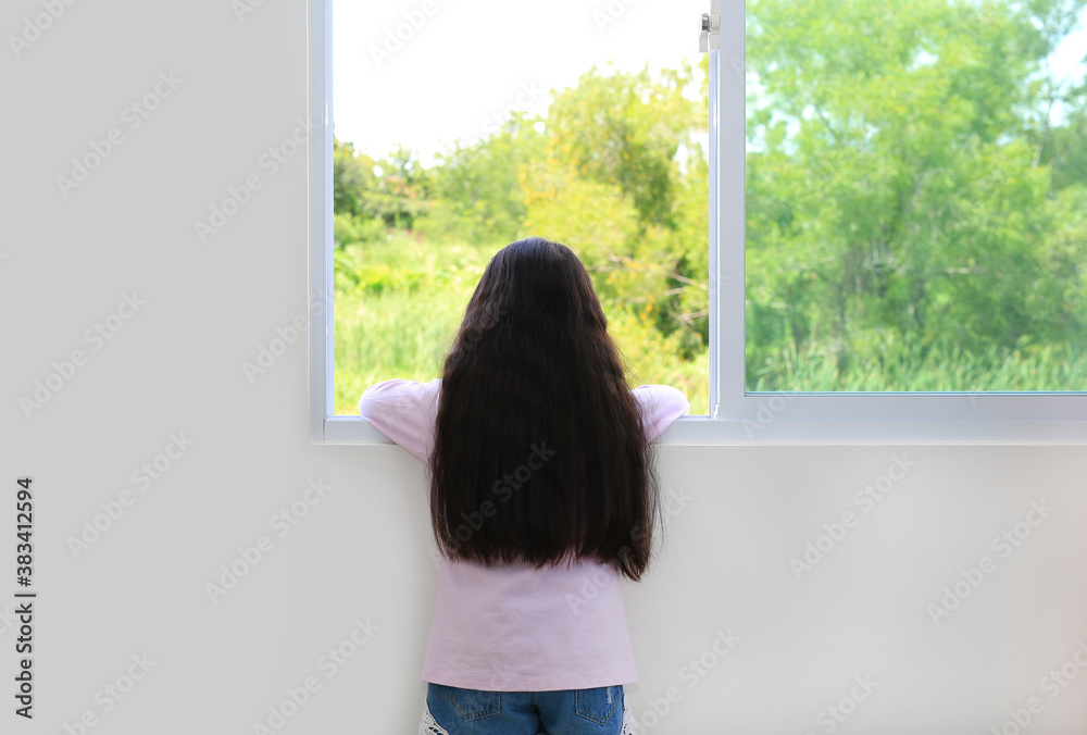 Caucasian little kid girl lies at window of house and watching out. Back view.
