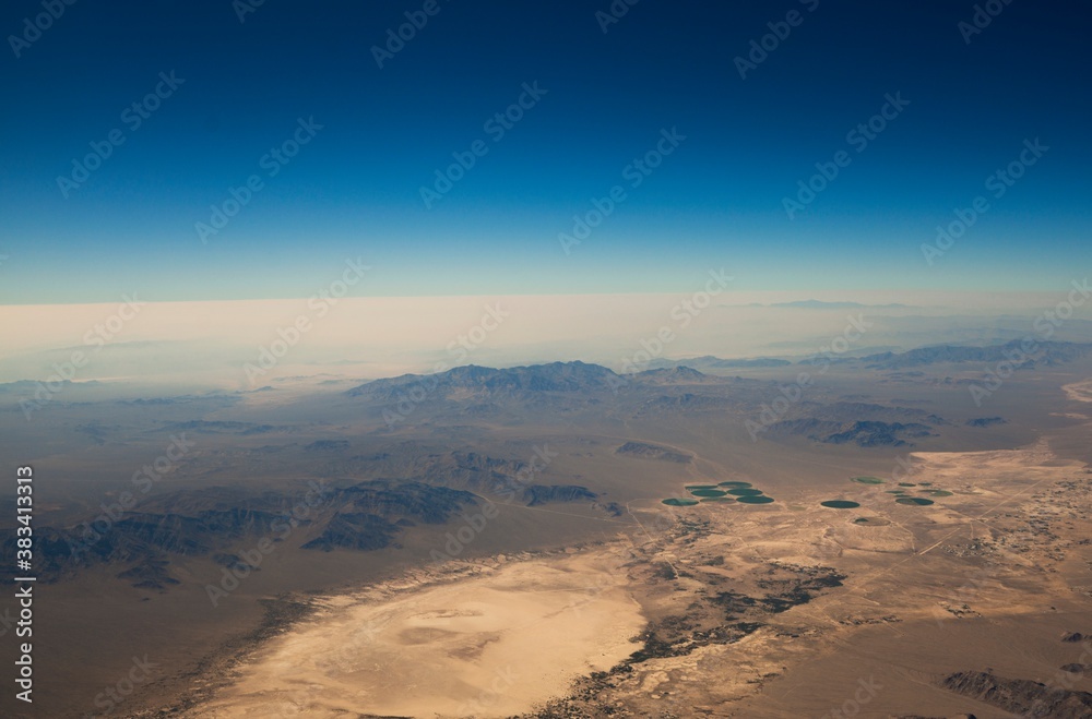 This image shows an aerial view of a vast desert landscape under a calm blue sky.