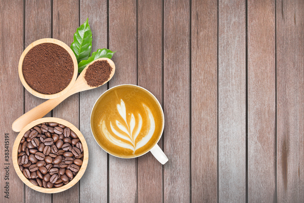 Coffee beans roasted in wooden bowl, Fresh coffee powder in bowl and in wooden spoon, Coffee leaves, Coffee latte in white ceramic mug, on wooden background. Coffee beans roasted in wooden bowl, Fresh coffee powder in bowl and in wooden spoon, Coffee leaves, Coffee latte in white ceramic mug, on wooden background.