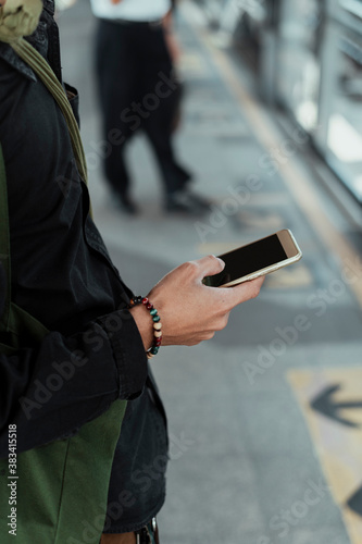 Close up hand of man using smartphone at train station.