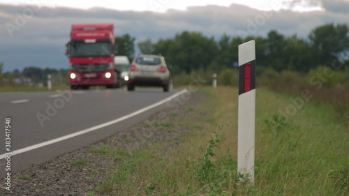 cars and a truck driving past the camera, a road sign in the foreground, a roadside shot. Transport outside the city, countryside