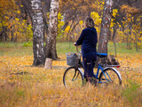 A girl in a blue suit in the autumn forest is walking next to a bicycle. Exercise bike on the slimming park.
